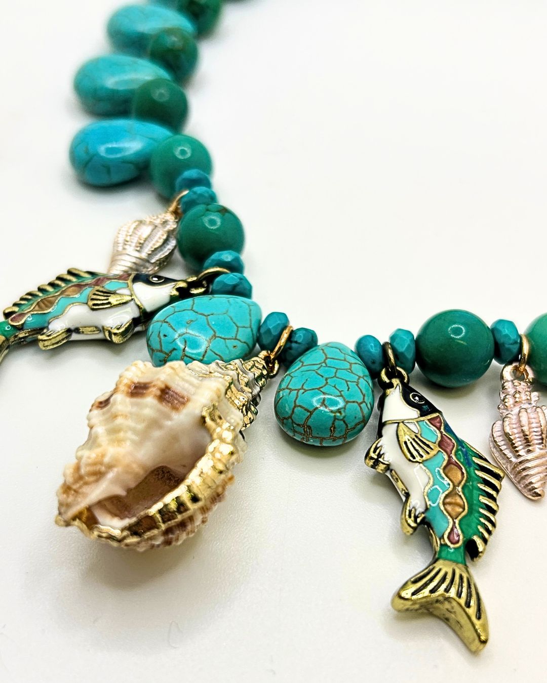 Close-up of enamel fish charms and a spiral shell charm among turquoise beads